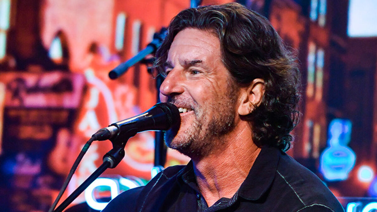 Grammy-winning songwriter of Jesus Take The Wheel performing live on stage with a microphone and smiling.