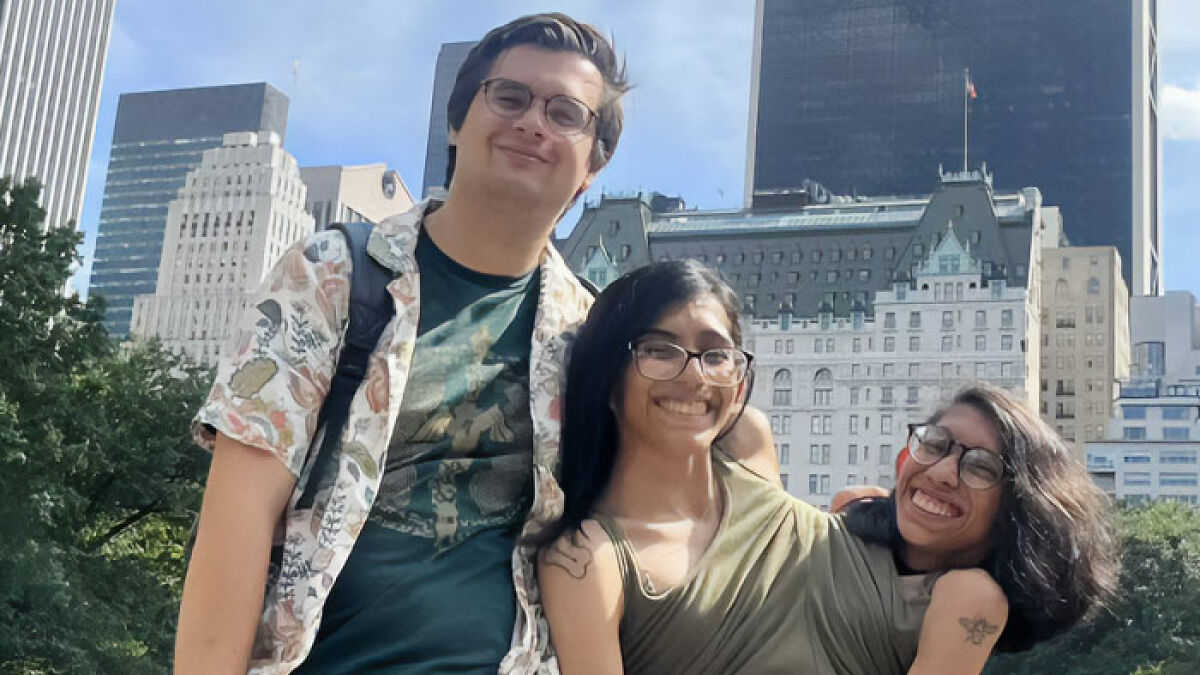 Conjoined twin Carmen Andrade smiling outdoors in a city setting with her husband and another person on a sunny day.