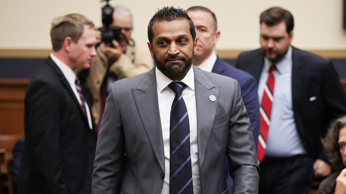 Man in gray suit and striped tie in a formal setting with others, related to FBI and Charlie Kirk conspiracy theories discussion.