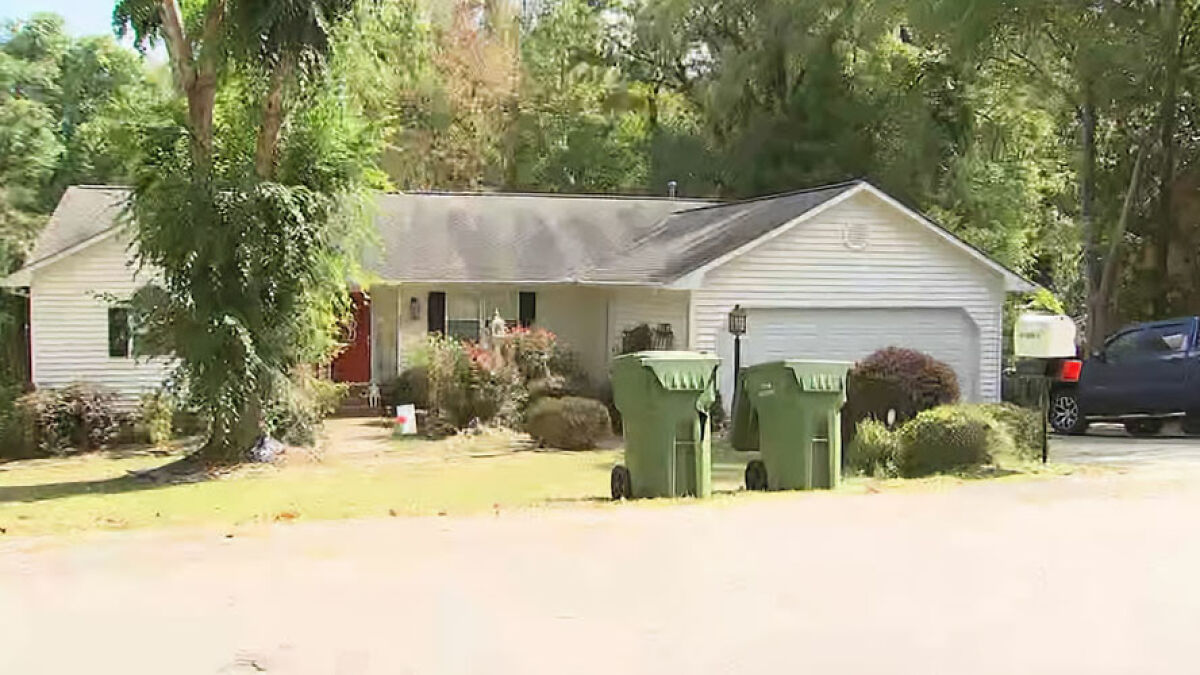 Suburban house with greenery and trash bins outside, linked to pastor's son accused of disturbing acts in basement captivity.
