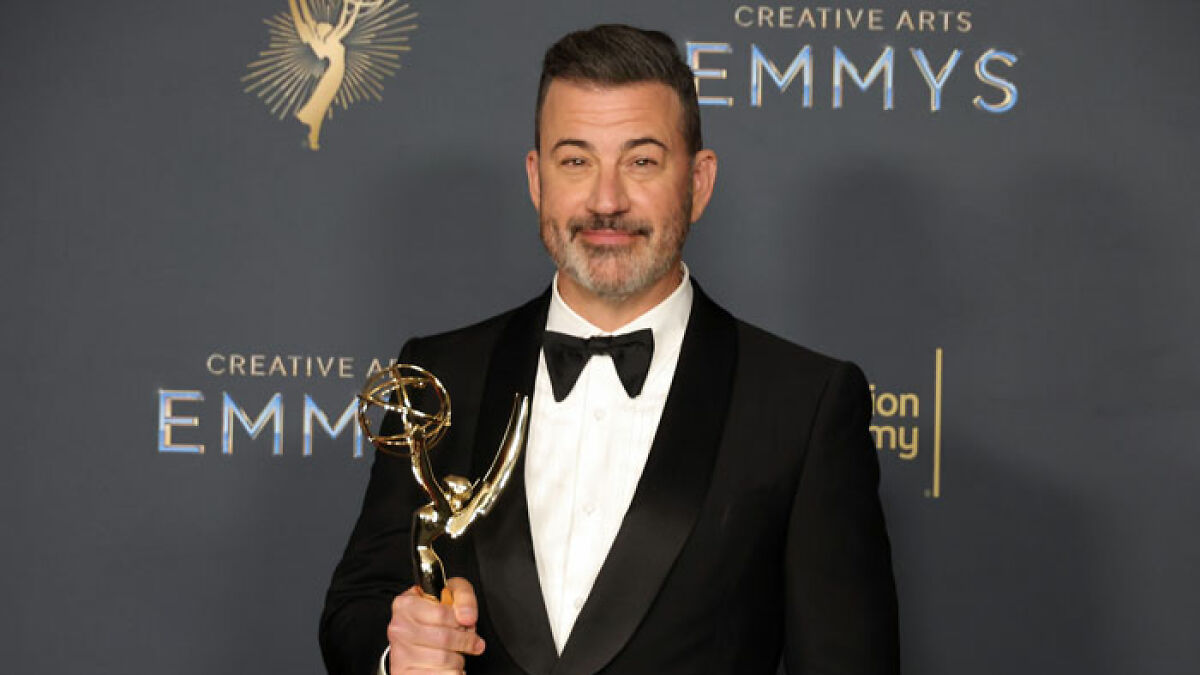 Jimmy Kimmel in a tuxedo holding an Emmy award at the Creative Arts Emmys event, smiling confidently.