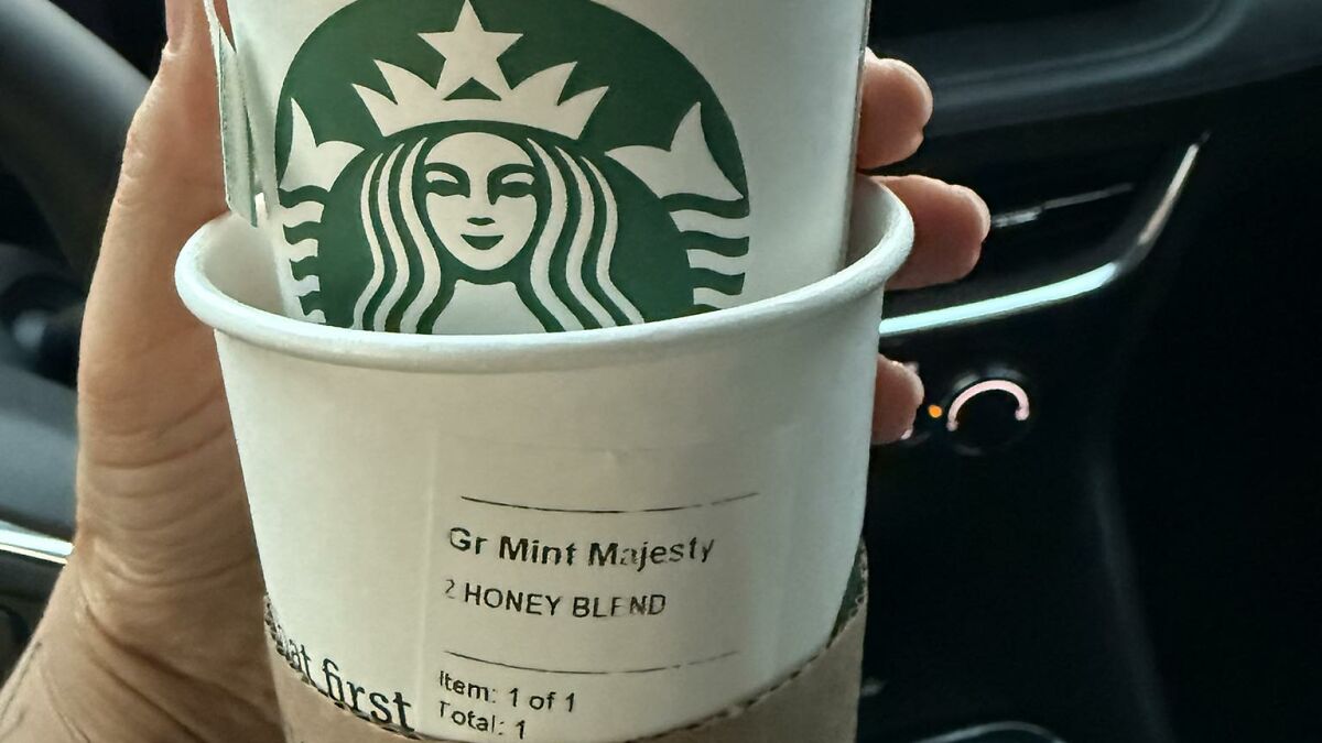 Hand holding Starbucks cup with Gr Mint Majesty drink label, highlighting hidden hate message on the cup inside a car.