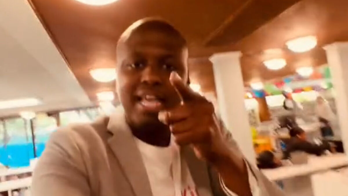 Black man confronting someone inside a library, pointing forward during a viral video capturing the tense moment.