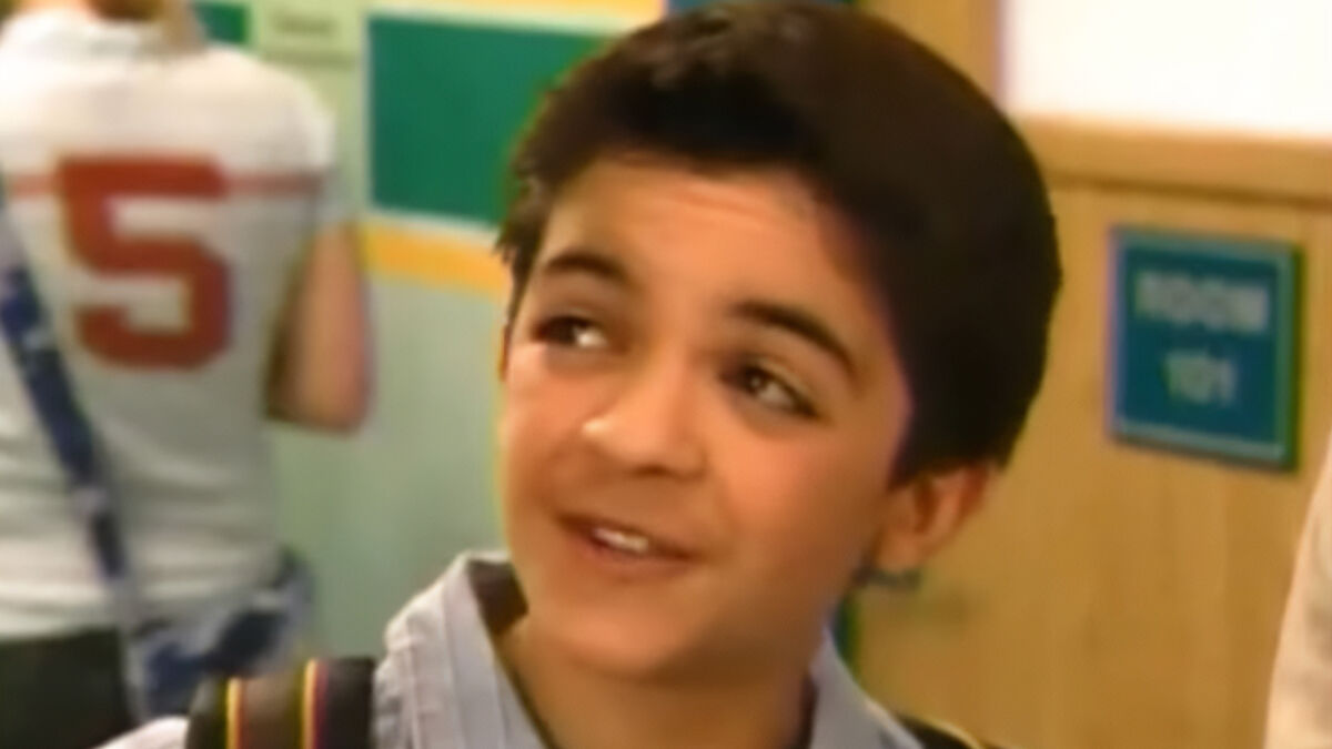 Former Nickelodeon child star as a young boy in a school hallway scene from a TV show or movie.