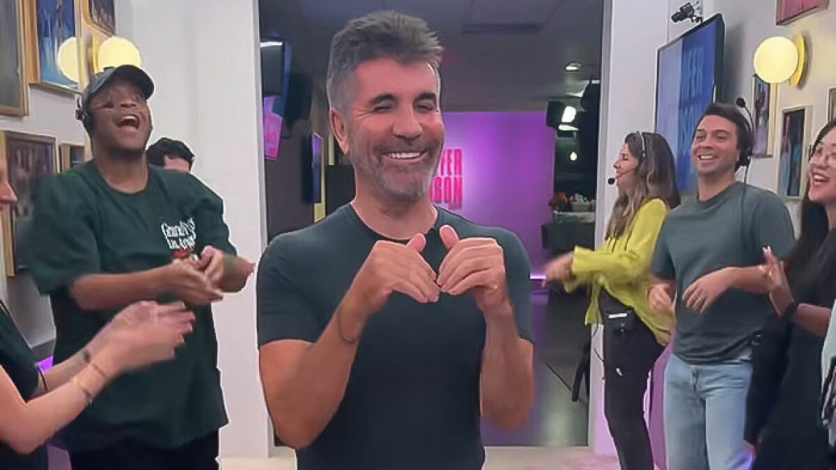 Simon Cowell smiling and clapping with a group of people in a studio setting, sparking viral concern after bike accident.