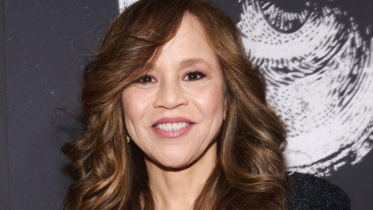 Rosie Perez smiling at an event, discussing Woody Harrelson's comment about her body during an intimate scene.