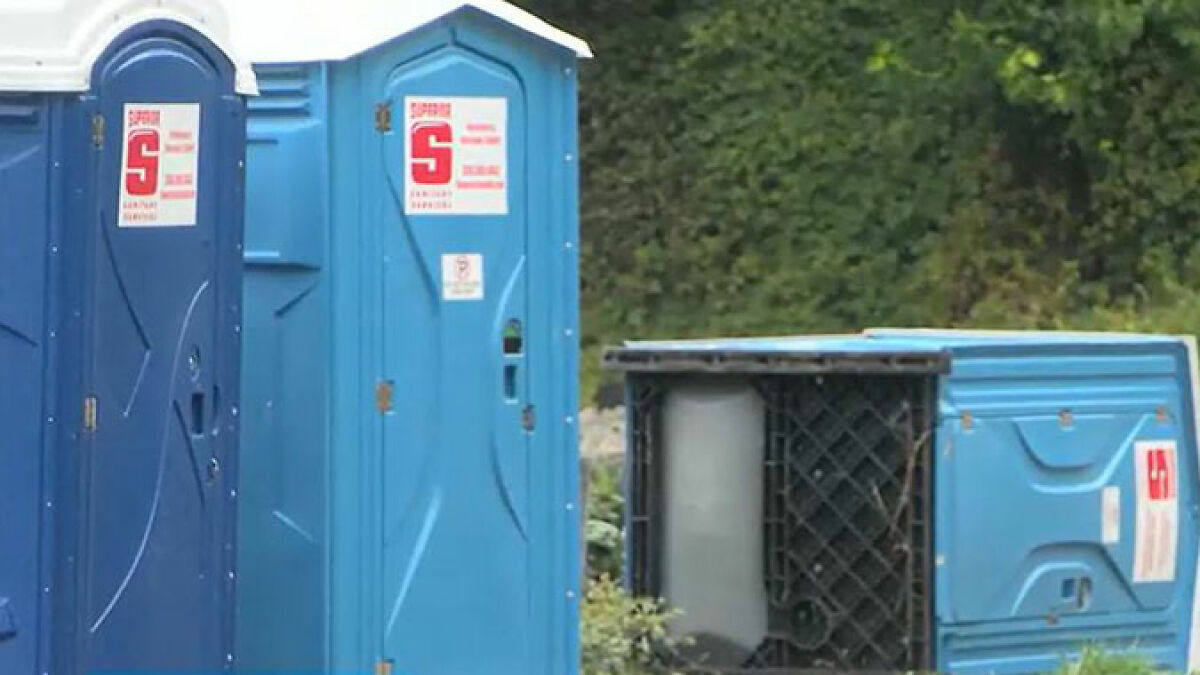 Blue portable toilets outdoors with one tipped over, related to cop opening fire over porta-potty prank incident.