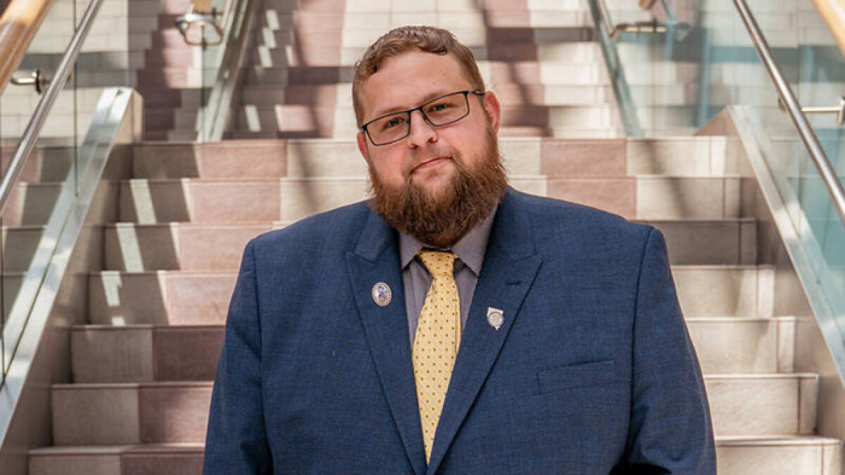 Man with beard and glasses wearing blue suit and yellow tie standing on steps, related to legal father of brother case.