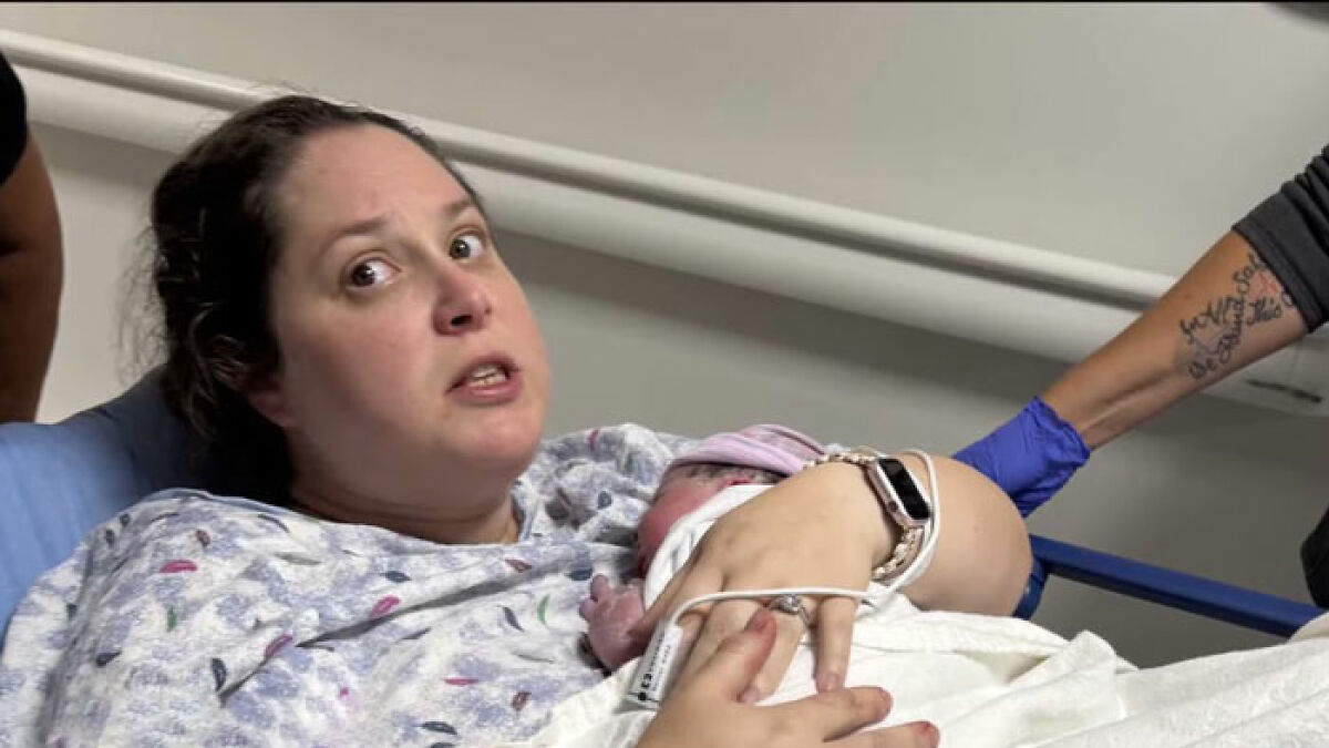 Woman holding newborn in hospital bed, surprised expression after unexpected pregnancy and delivery of third child.