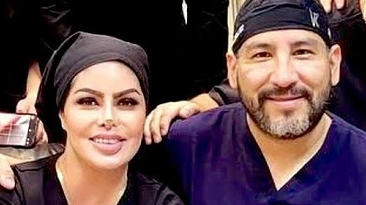 Surgeon and woman seated together, both wearing dark head coverings and smiling at the camera.