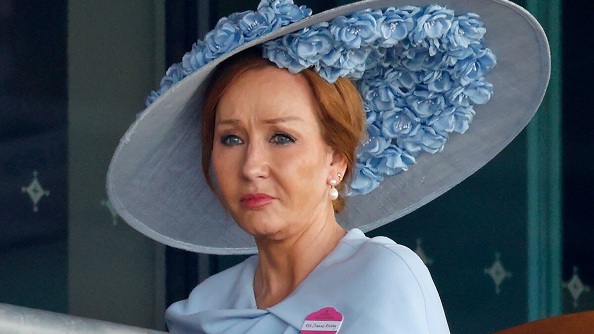 J.K. Rowling wearing a large blue floral hat, reacting with a serious expression during a public event.