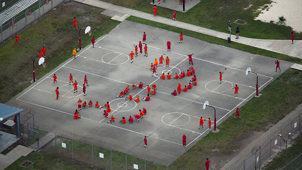Aerial view of detainees in orange and red uniforms on fenced basketball courts at an ICE detention center known as Alligator Alcatraz.