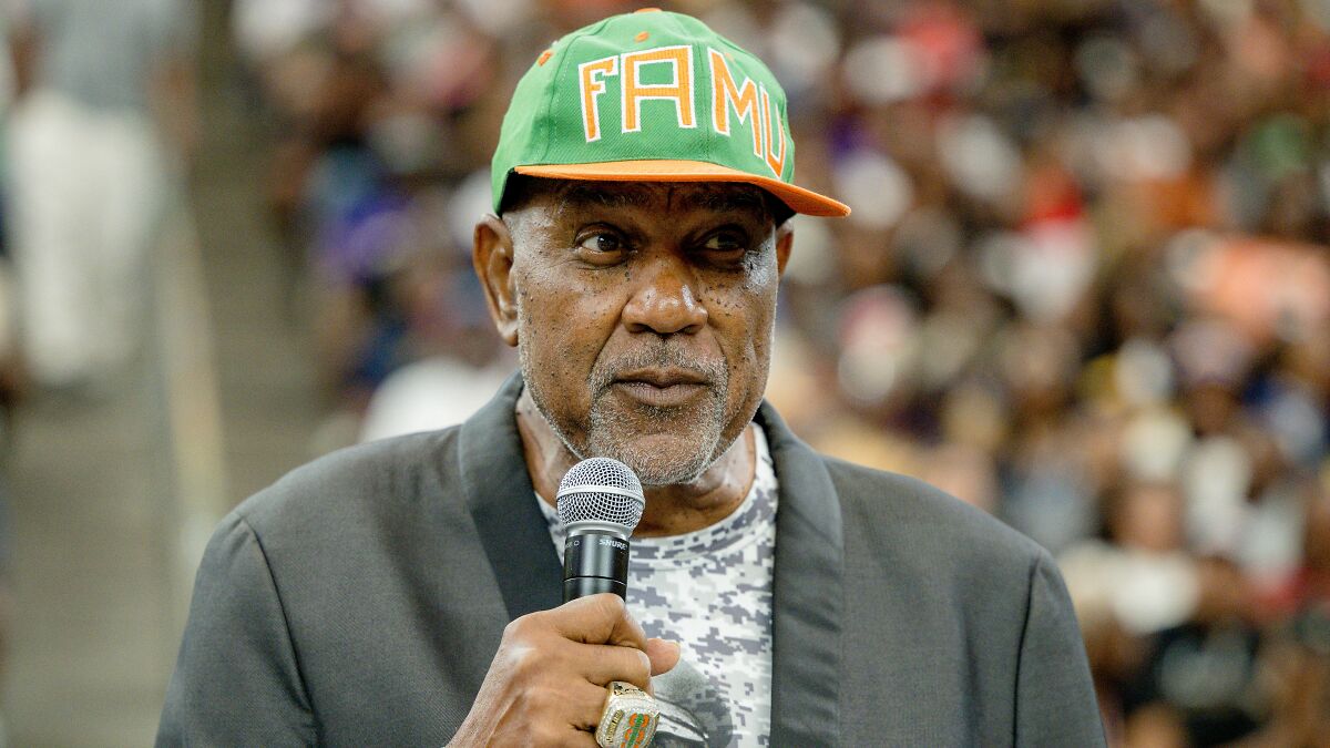 College band announcer wearing FAMU hat holds microphone during halftime performance amid backlash over bodyshaming plus-size dancers.