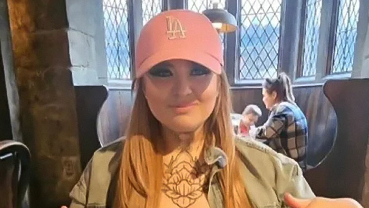 Woman wearing pink LA hat and green jacket sitting indoors with people in the background, related to American nightmare mom story