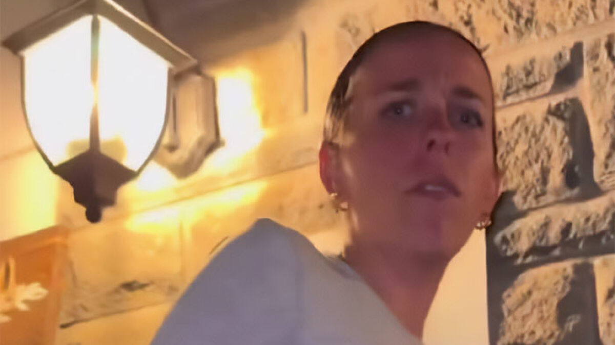 Woman exposing new bride for cheating during wedding week, standing near a lit outdoor wall lamp at night.