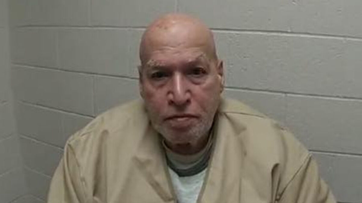 Man in beige jacket sitting against a gray brick wall, related to police solving brutal cold case after 52 years.