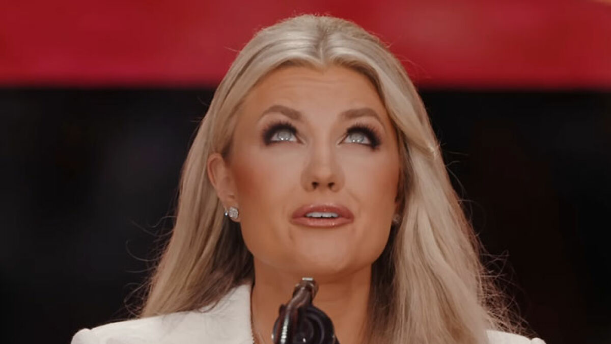 Blonde woman speaking intently into microphone with red and black background, Elon Musk hypocrisy topic.