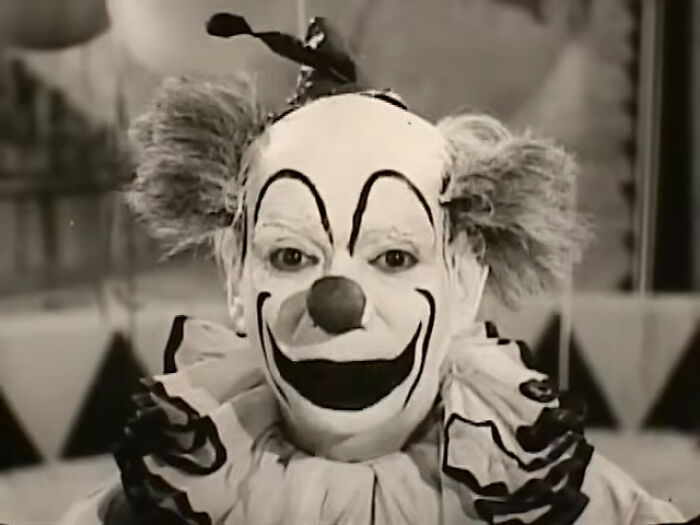 Black and white image of a creepy clown with exaggerated makeup and wild hair, evoking nightmares from commercials.