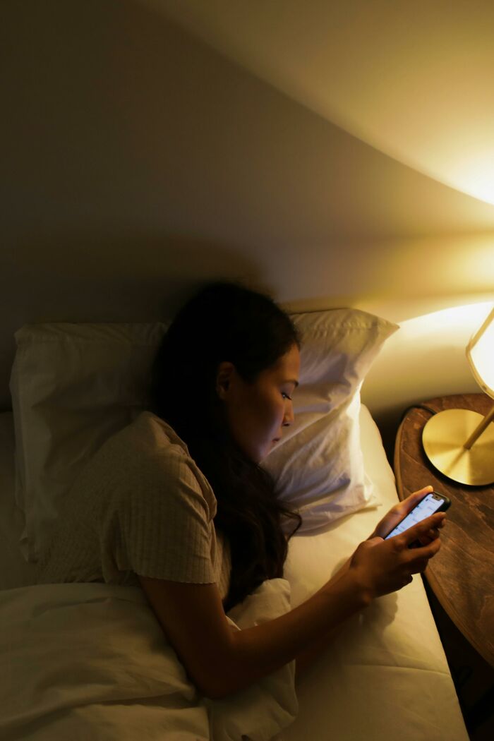 Person lying in bed at night, looking at phone screen, surrounded by warm light, depicting bizarre messages and phone calls.
