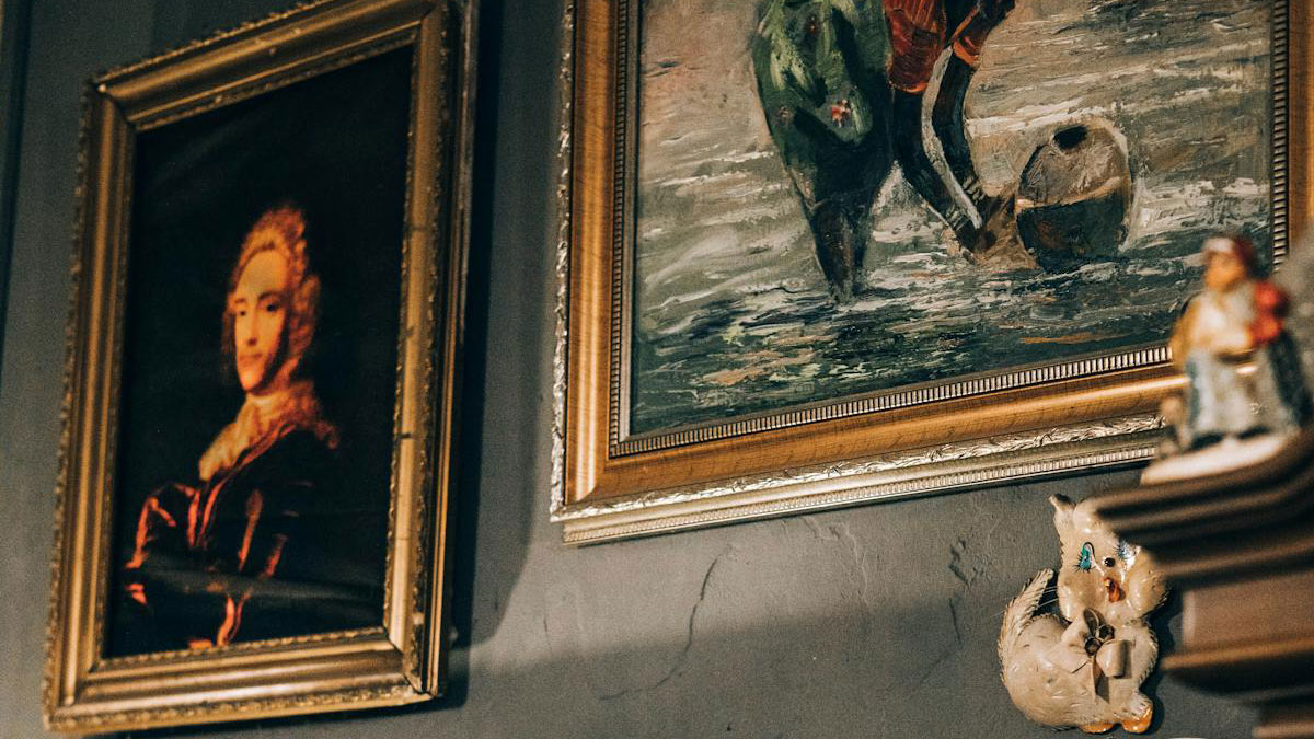 Two framed paintings on a wall with dim lighting creating a creepy atmosphere for dark woods stories.