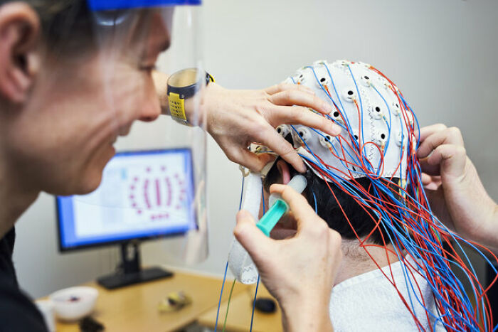 Scientist fitting a brain monitoring cap with electrodes on a person, exploring gut feeling and precognition research. Scientist fitting a brain monitoring cap with electrodes on a person, exploring gut feeling and precognition research.