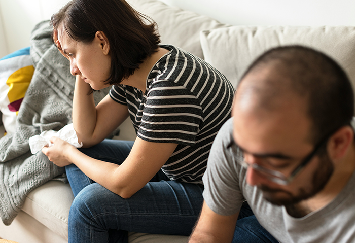 Upset father and mother sitting on couch discussing their son's suspension after teacher scares student in class incident. Upset father and mother sitting on couch discussing their son's suspension after teacher scares student in class incident.