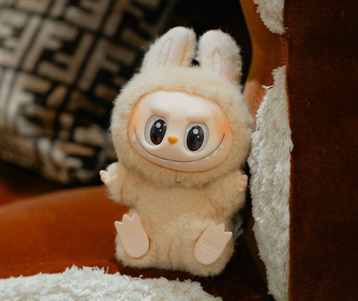 Fluffy toy in bunny costume with big eyes sitting on a brown couch, representing overhyped products concept.