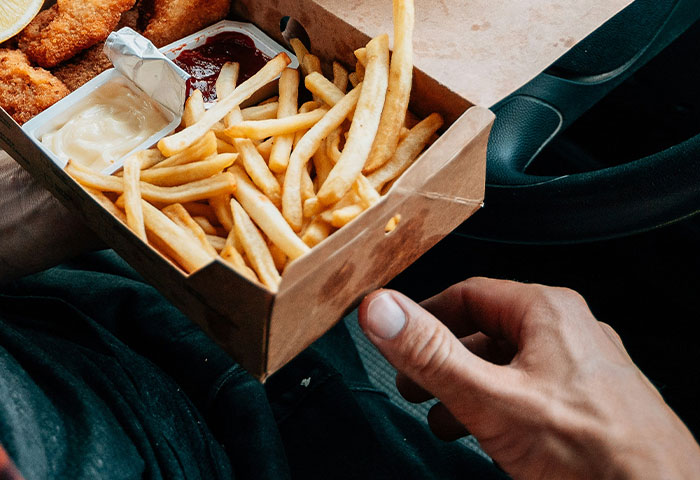 Person holding a box of fast food fries and sauces inside a car, illustrating poor hygiene habits causing partners to gag.