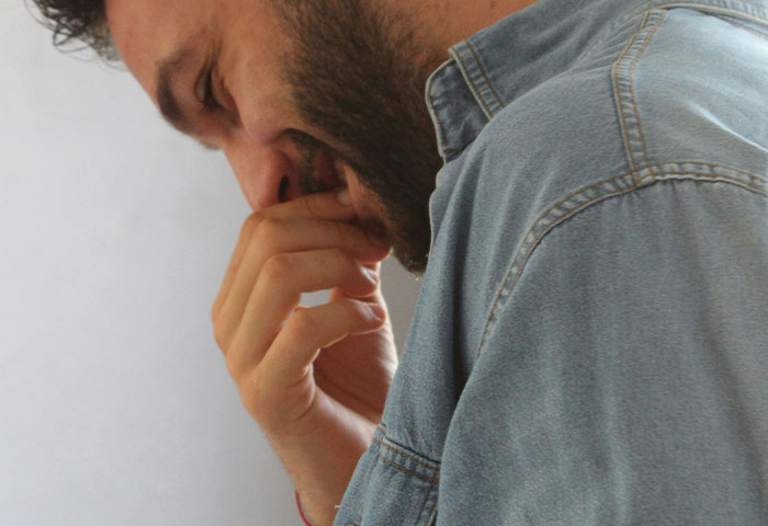 Man in denim shirt holding nose with hand, showing reaction to bad hygiene causing gagging in close-up profile.