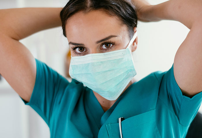 Woman wearing a medical mask and teal scrubs, emphasizing hygiene concerns in a clinical setting related to bad hygiene issues.