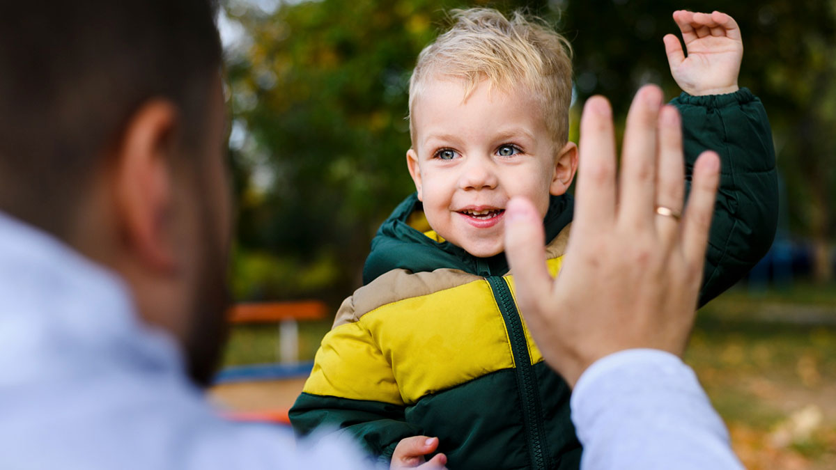 Young boy giving a high five to man outdoors, illustrating family drama involving financial support and stepbrother conflict.