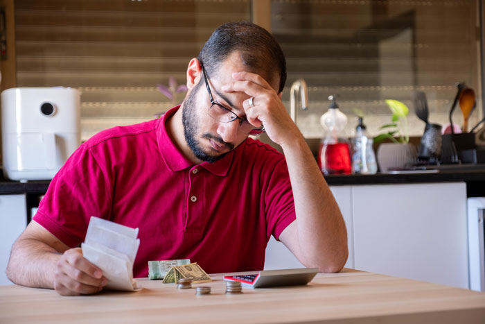 Man in red shirt stressed while counting money and bills, highlighting stepbrother financial support drama for pregnant girlfriend.