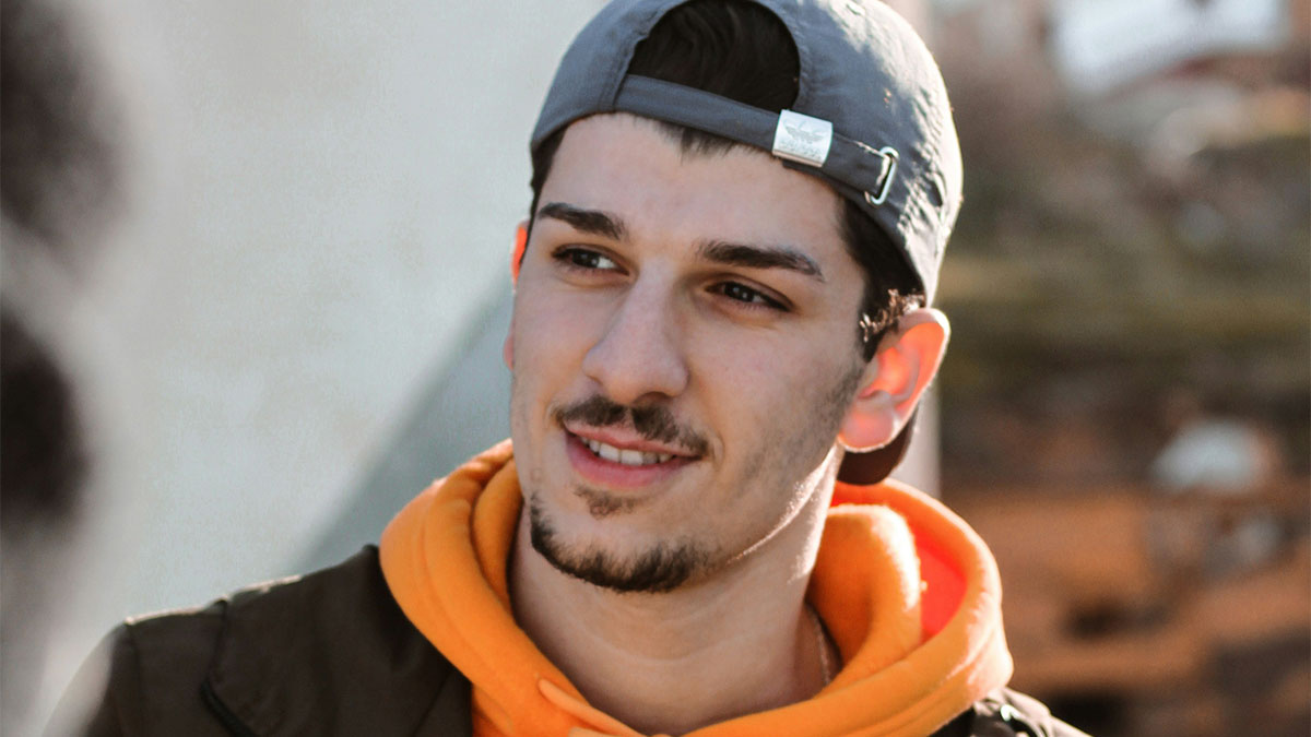 Young man in a backward cap and orange hoodie, smiling outdoors, representing landlord finally getting rid of horrible tenants.