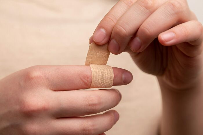 Close-up of hands applying bandage on finger, illustrating a moment of care in a setting fit for creepy stories in the dark woods. Close-up of hands applying bandage on finger, illustrating a moment of care in a setting fit for creepy stories in the dark woods.