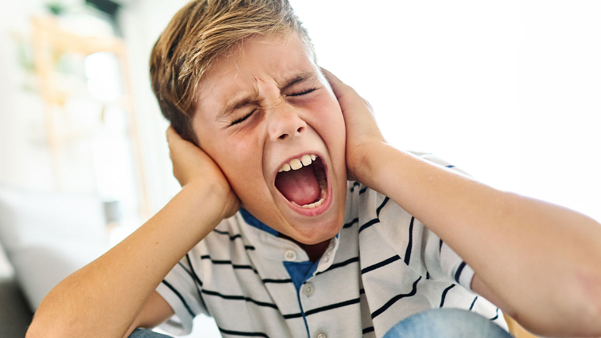 Young boy having a meltdown covering ears indoors, expressing frustration about mountain biking early in the morning.