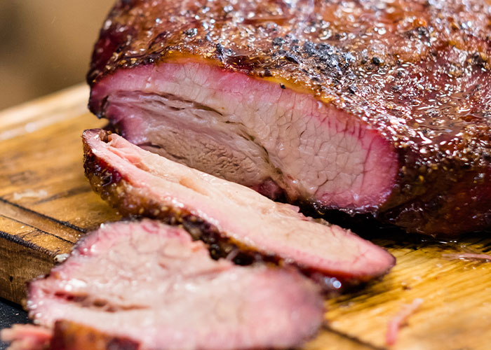 Close-up of sliced smoked brisket with a crispy crust on a wooden cutting board, showcasing food industry quality.