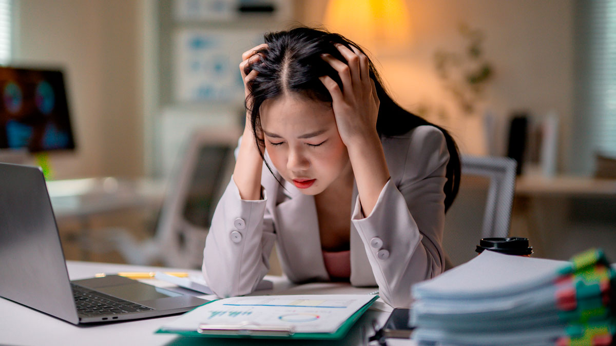 Stressed employee at desk holding head, struggling with work after sick leave, illustrating reasons to quit job.