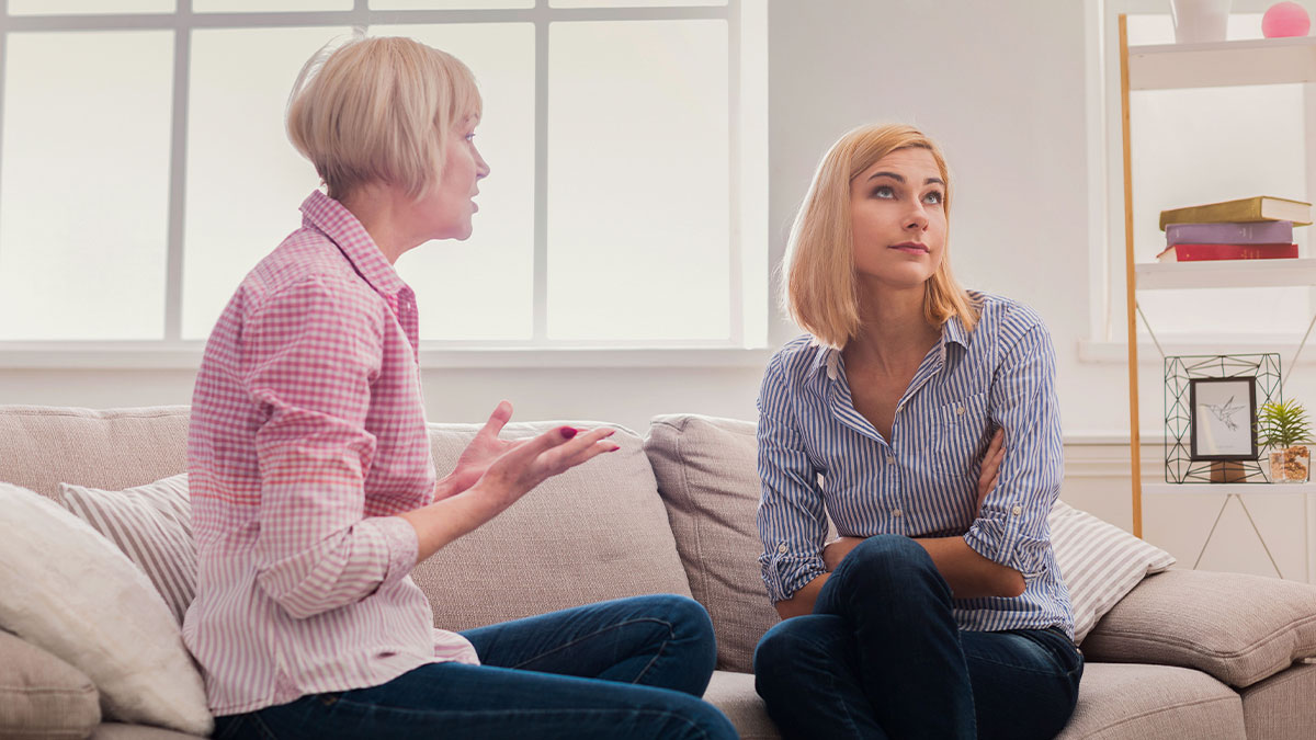 Mom and 20-year-old sister sitting on couch discussing childcare and babysitting responsibilities at home.