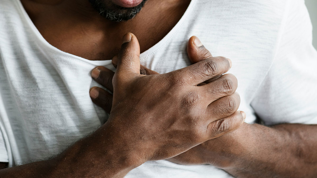 Man in white shirt clutching chest in pain, illustrating healthcare workers shared life-threatening stories.