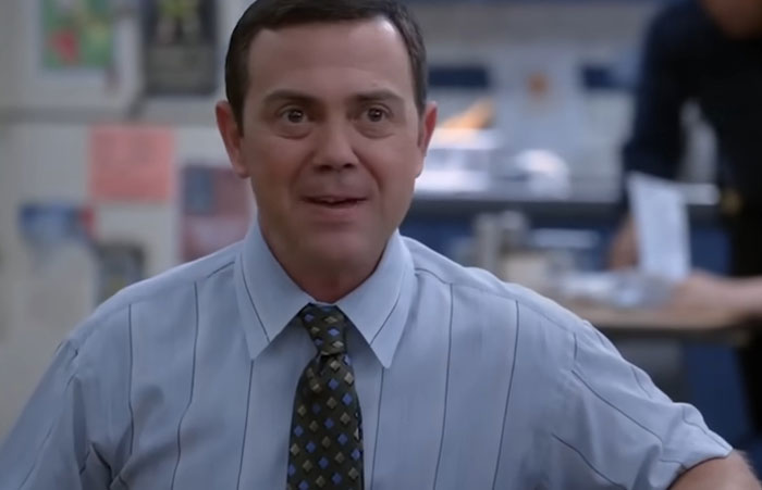Man in a blue shirt and patterned tie speaking in an office setting sharing healthcare workers stories.