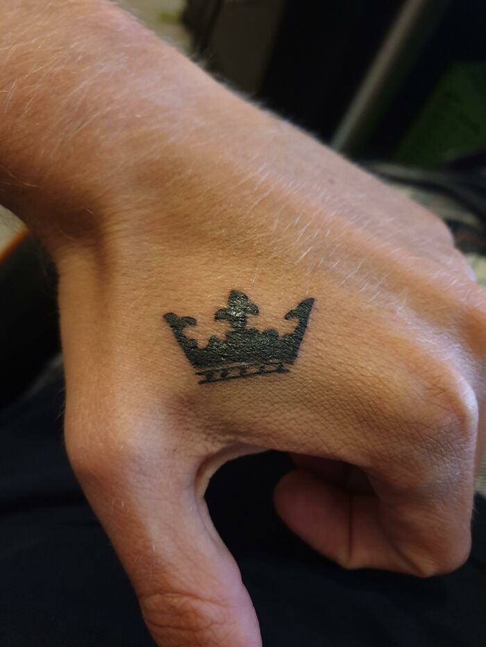 Small black crown tattoo on the back of a hand, illustrating unusual client tattoo requests by artists.