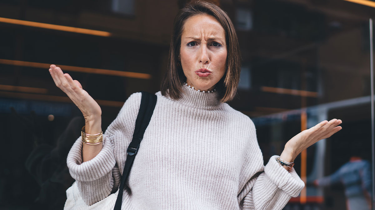 Woman in a beige sweater showing frustration outside a building, expressing confusion and disbelief during an unwanted visit.