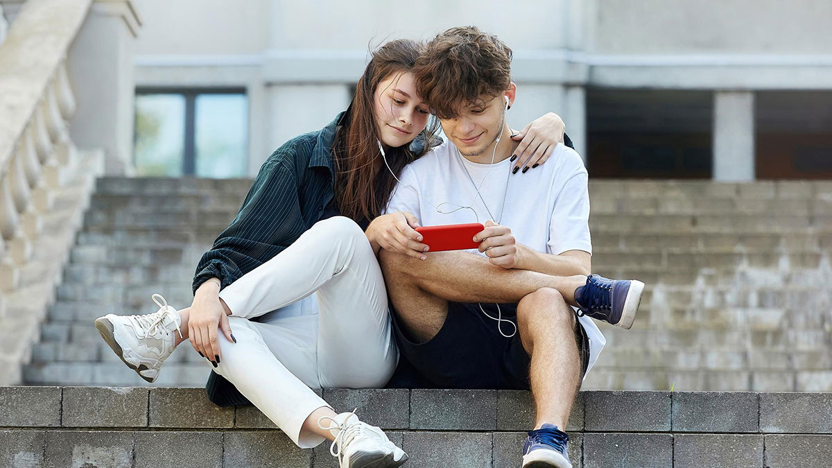 Teen couple sitting on steps sharing earbuds and watching a phone, depicting dating and love nest conflict with stepdaughter.