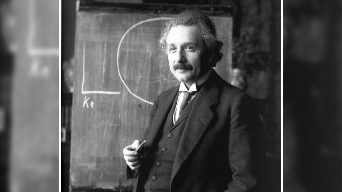 Black and white photo of a man in a suit holding chalk, standing in front of a chalkboard illustrating so-called facts about history.