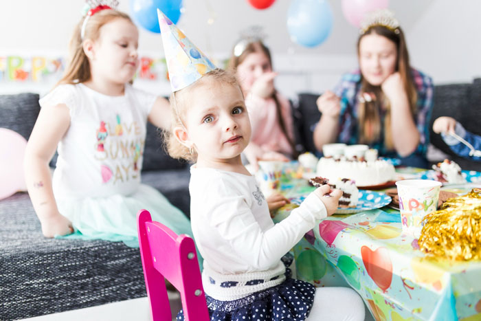 Young girl in party hat sitting at decorated table with cake, illustrating family event where lady stands up for cousin's wife against rude hubby. Young girl in party hat sitting at decorated table with cake, illustrating family event where lady stands up for cousin's wife against rude hubby.