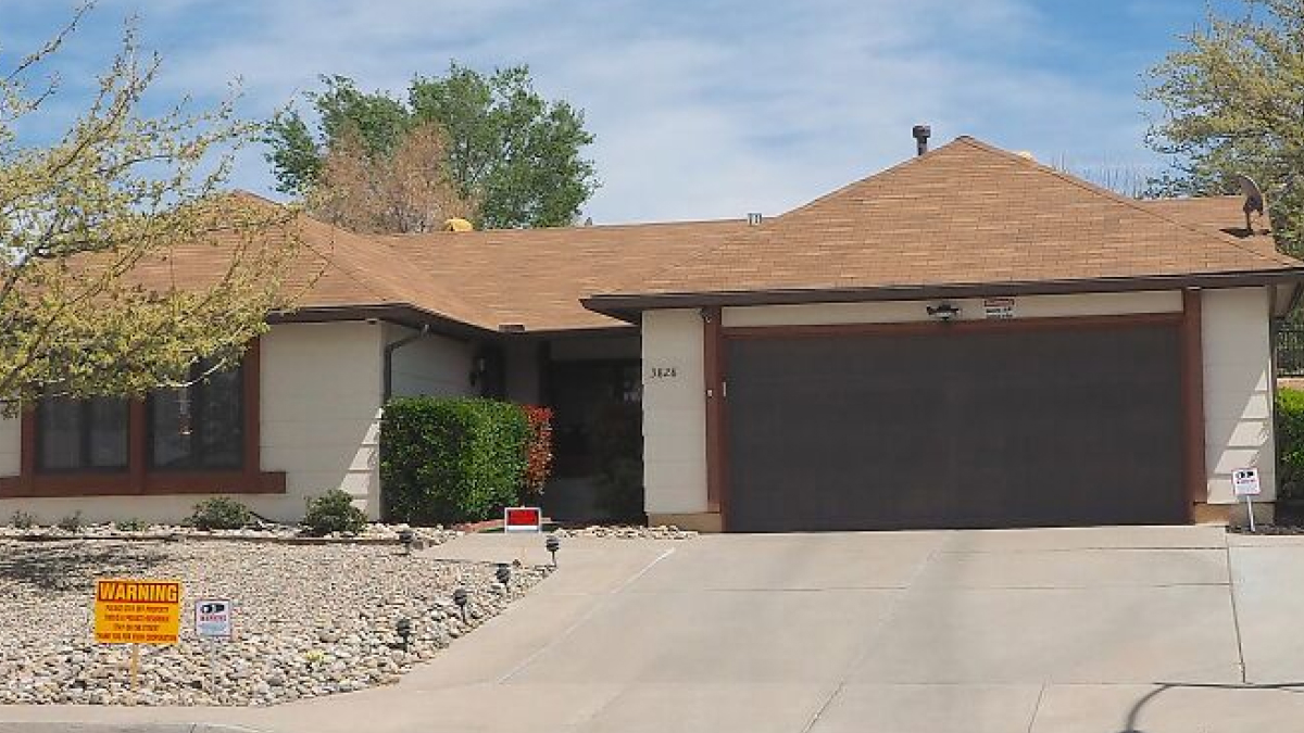 Single-story iconic TV house with beige exterior, brown roof and garage, surrounded by rocks and trees in a suburban setting