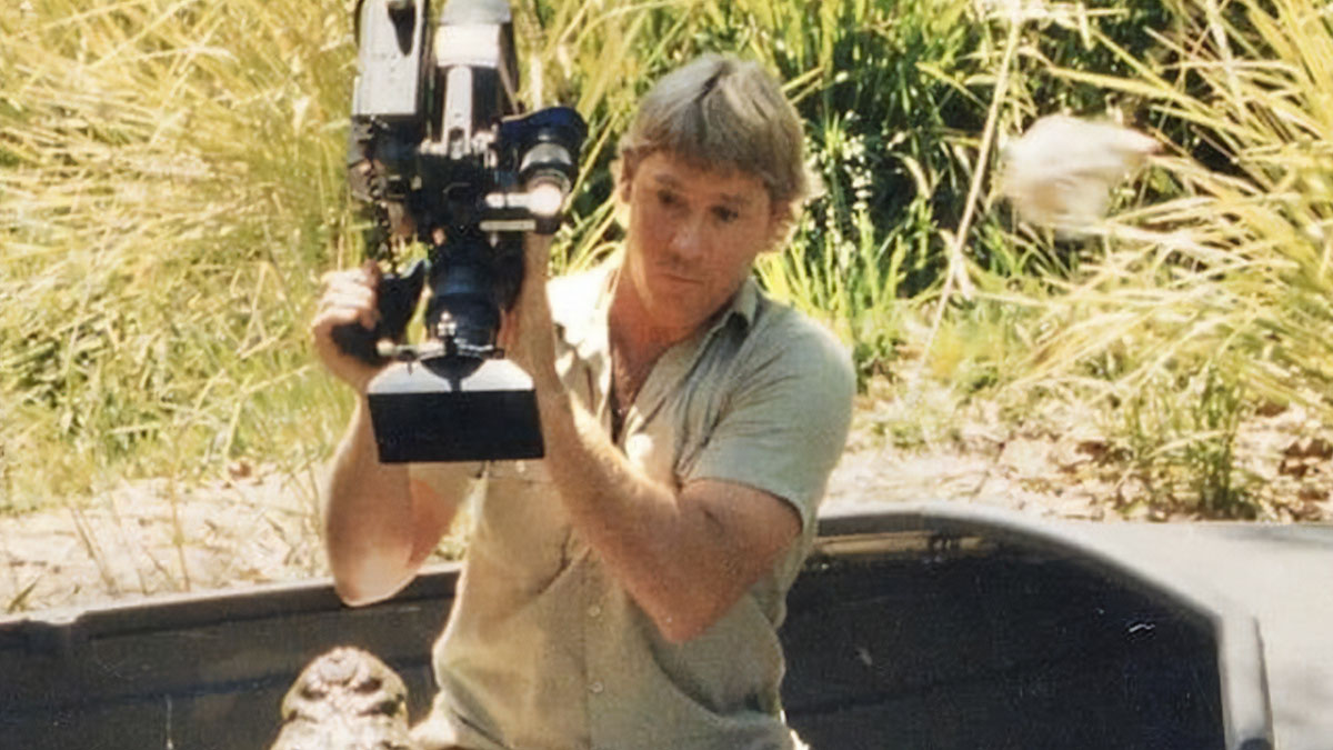 Wildlife cameraman filming in a natural setting, related to famous people who have lost their lives in animal attacks.