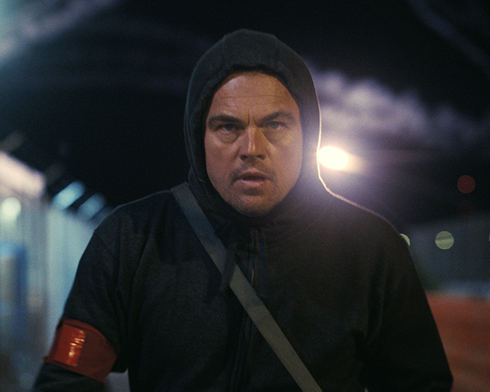 Leonardo DiCaprio in a dark hoodie running outdoors at night with an intense expression and steam in the background. Leonardo DiCaprio in a dark hoodie running outdoors at night with an intense expression and steam in the background.