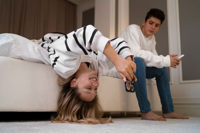 Two siblings in a bedroom, a girl playing with her phone upside down while her brother watches, reflecting child support dynamics. Two siblings in a bedroom, a girl playing with her phone upside down while her brother watches, reflecting child support dynamics.