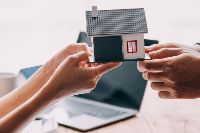 Two people holding a miniature house model representing 50/50 ownership in a home purchase agreement. Two people holding a miniature house model representing 50/50 ownership in a home purchase agreement.
